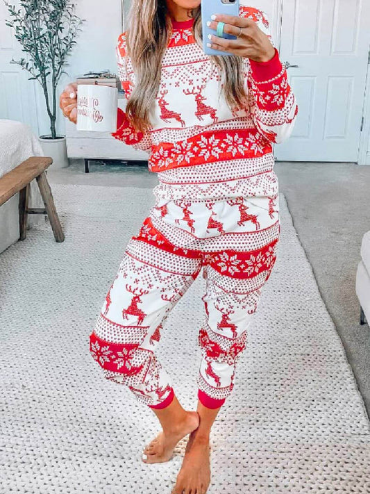 Cozy woman in Christmas 2 Piece Pajamas with reindeer print, enjoying a holiday beverage in a festive home setting.