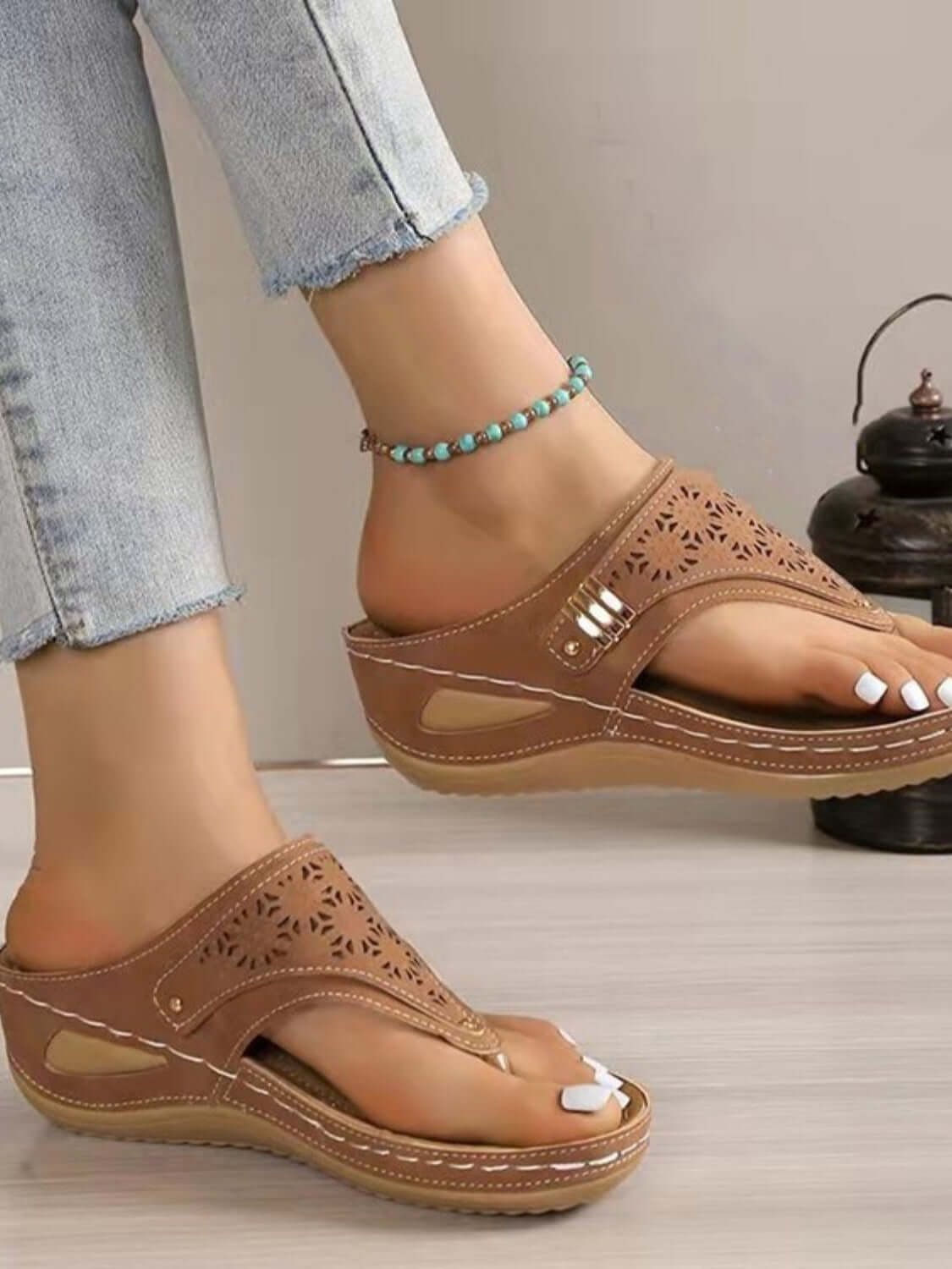 Stylish brown sandals with cutout design, paired with light jeans and a beaded anklet, perfect for summer vibes.