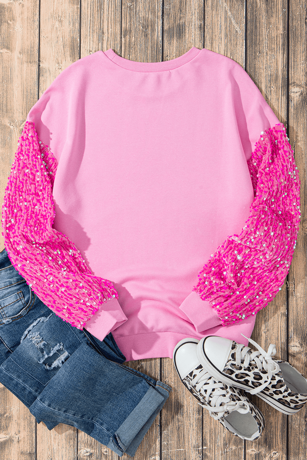 Back view of a pink Sequin Heart Sweatshirt paired with distressed jeans and stylish sneakers on a wooden surface.